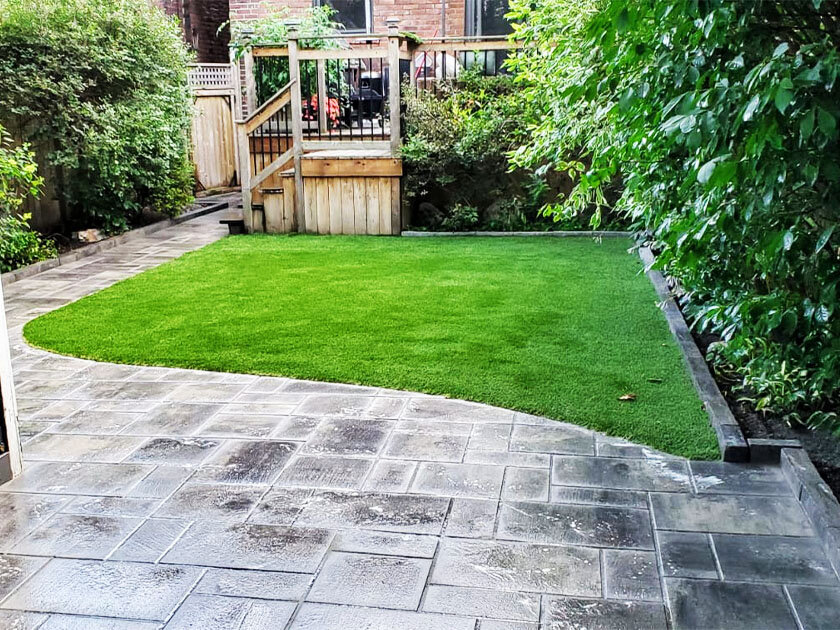 Beautiful, synthetic turf in backyard with stone path surrounding it.